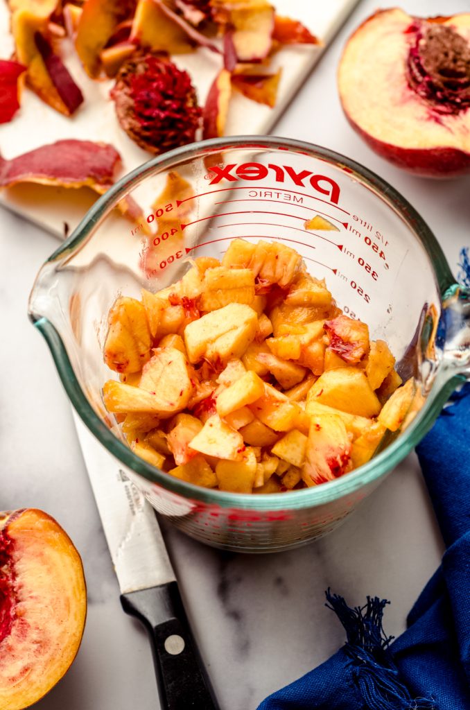A measuring cup full of chopped peaches.