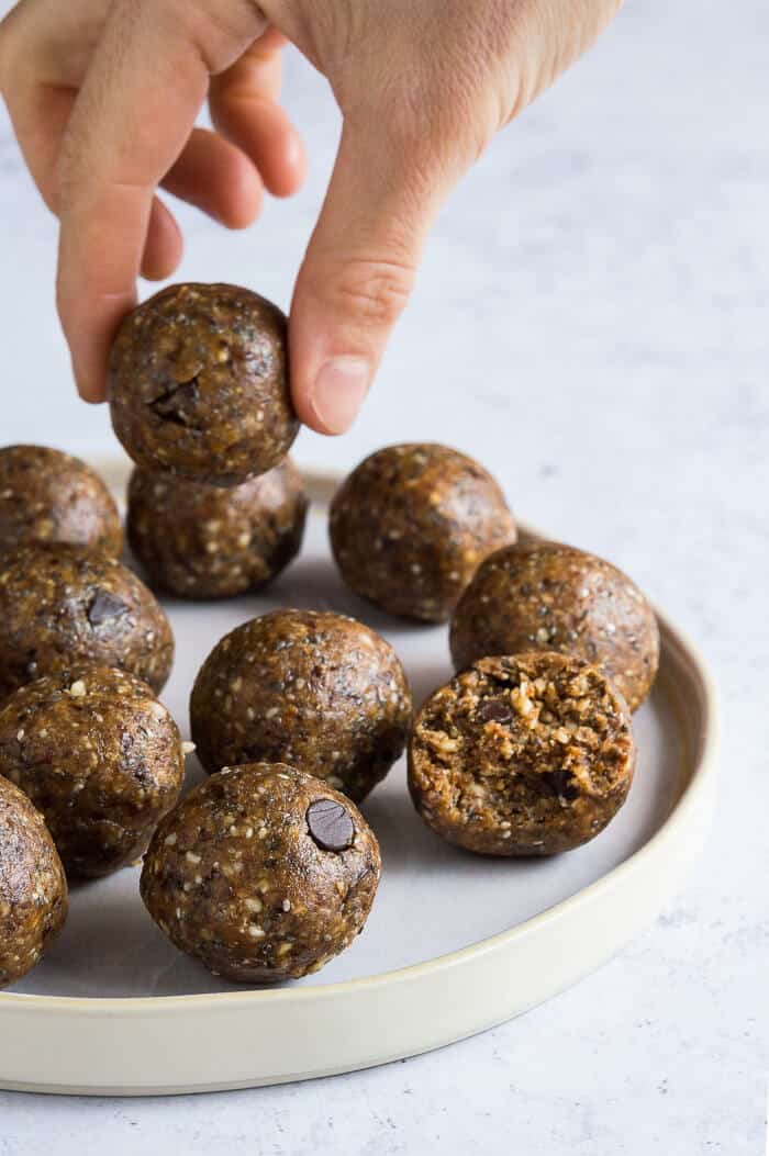 Chocolate chip peanut butter energy balls on a white plate with a hand picking one up.