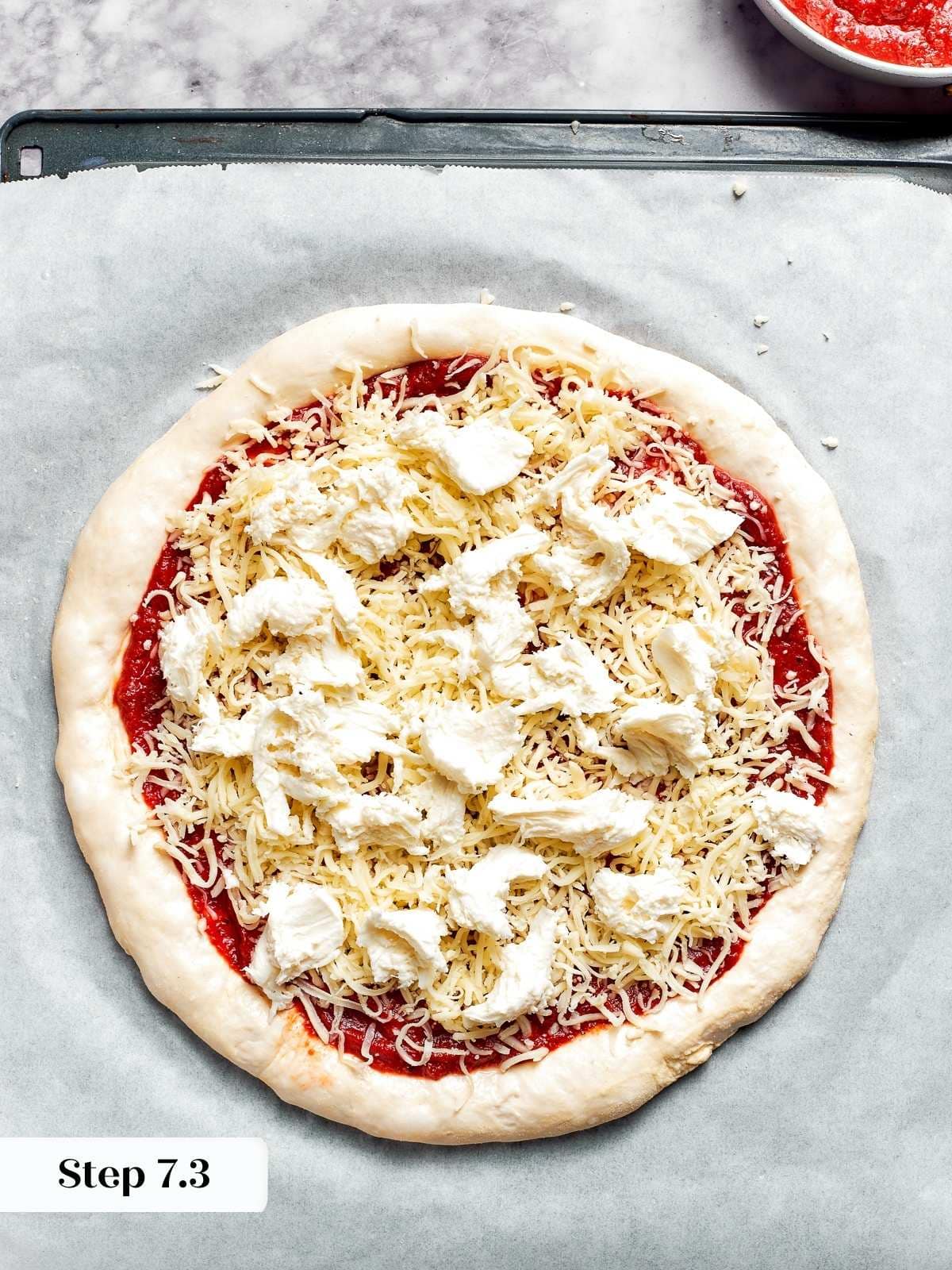 Topping the pizza dough with fresh mozzarella before baking.