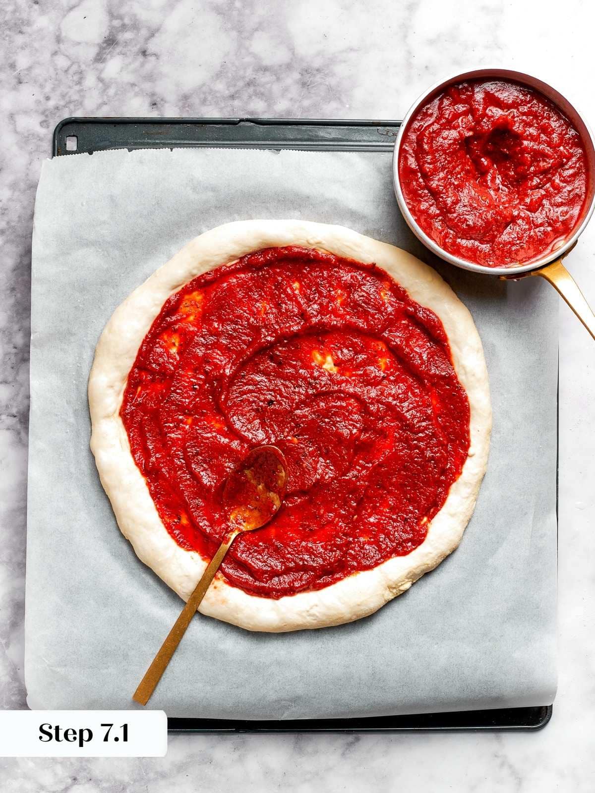 Tomato pizza sauce being spread onto round pizza dough.