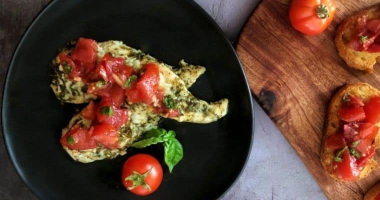pesto chicken with bruschetta on top and a cutting board with bruschetta on a baguette