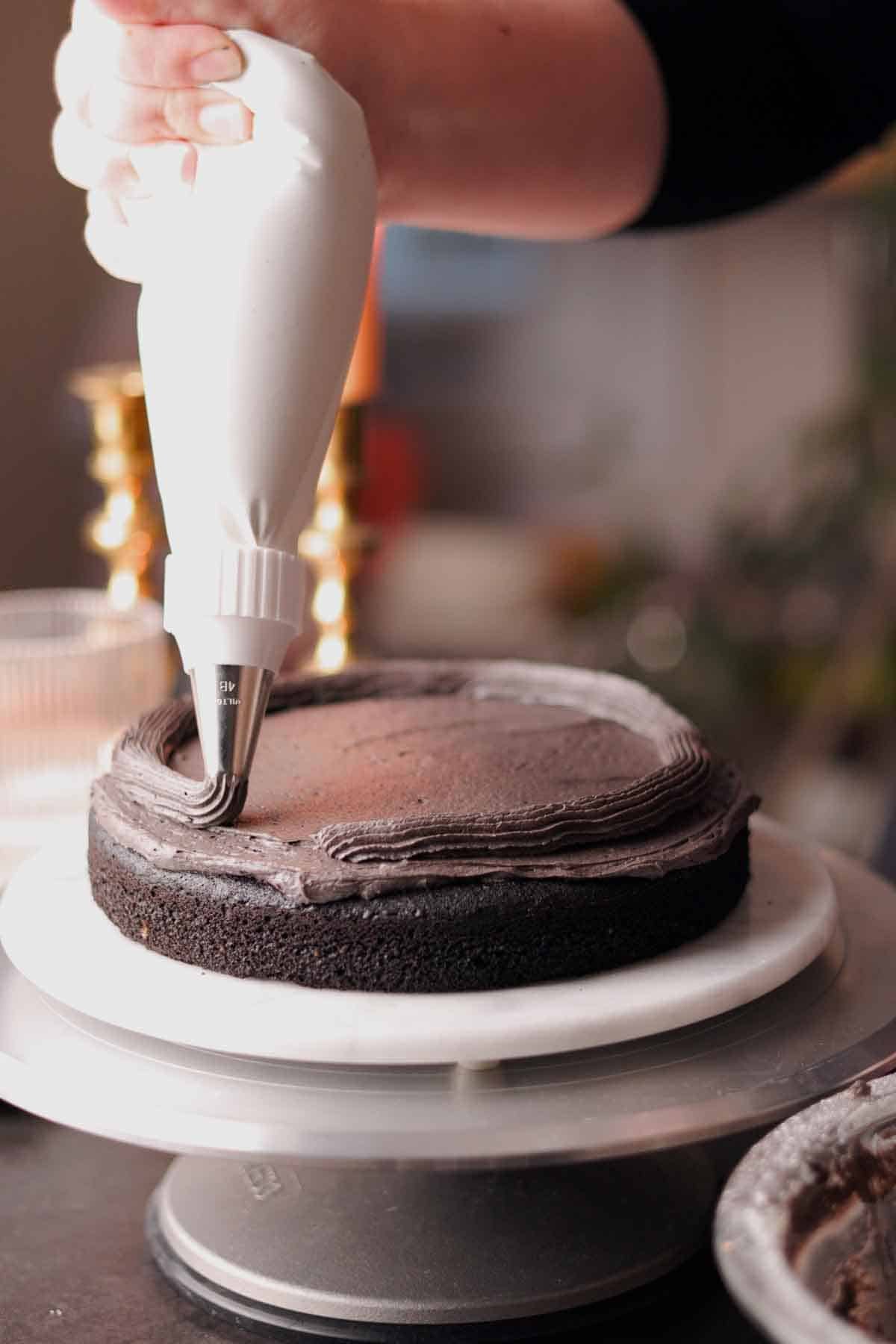 piping a border of black frosting on a round cake layer