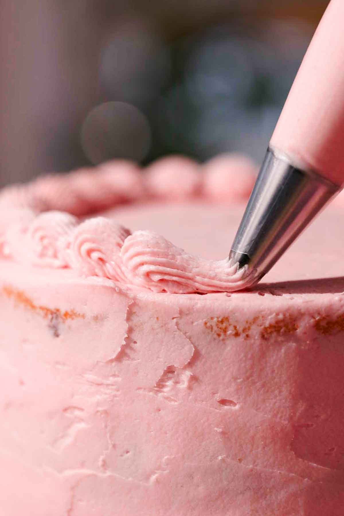 piping a border of pink frosting using an open star piping tip