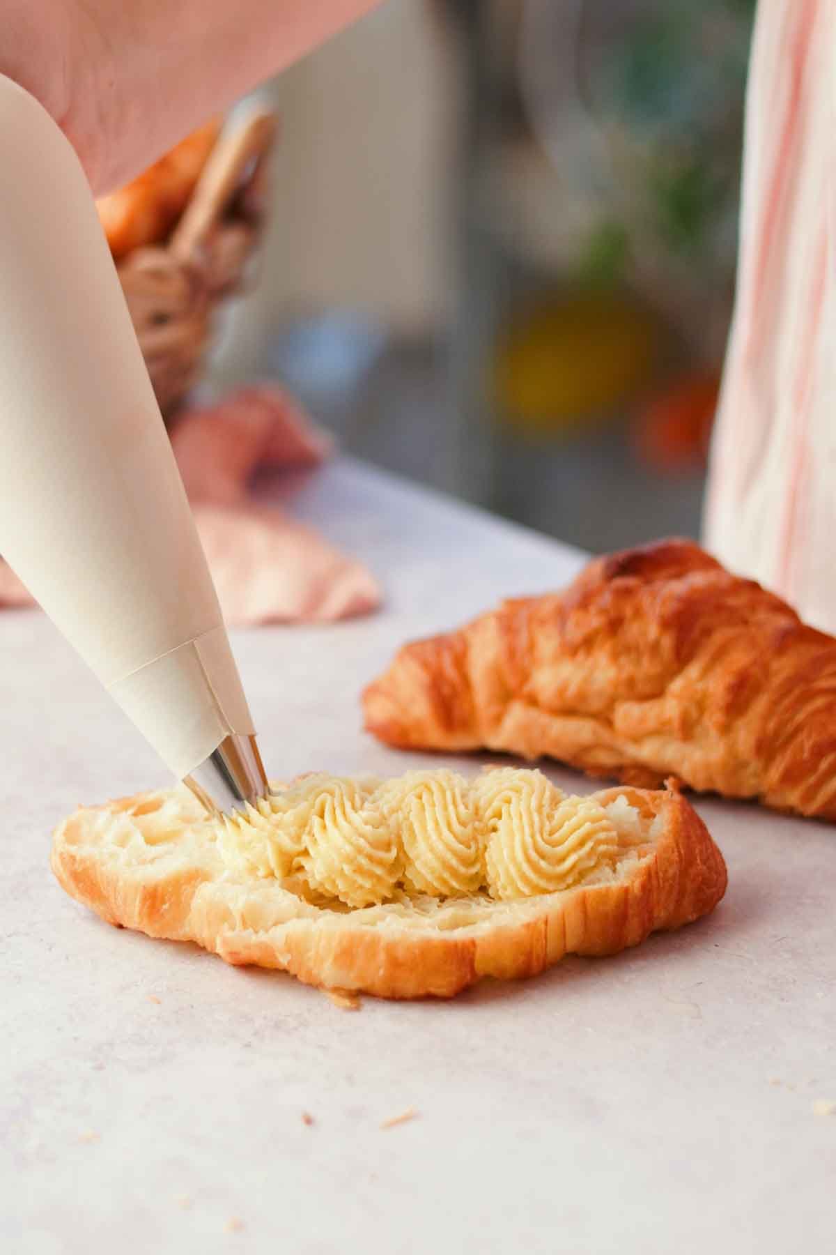 piping almond frangipane filling inside of croissant with piping bag