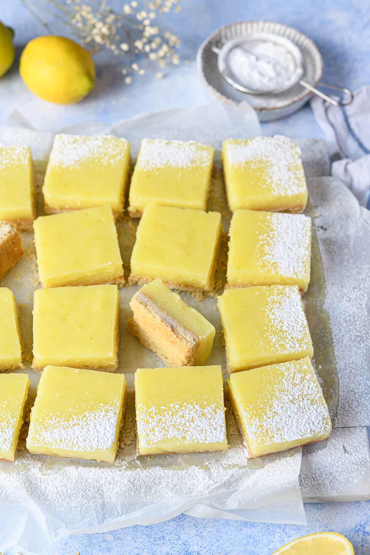 Lemon bars on white baking parchment on a blue surface.