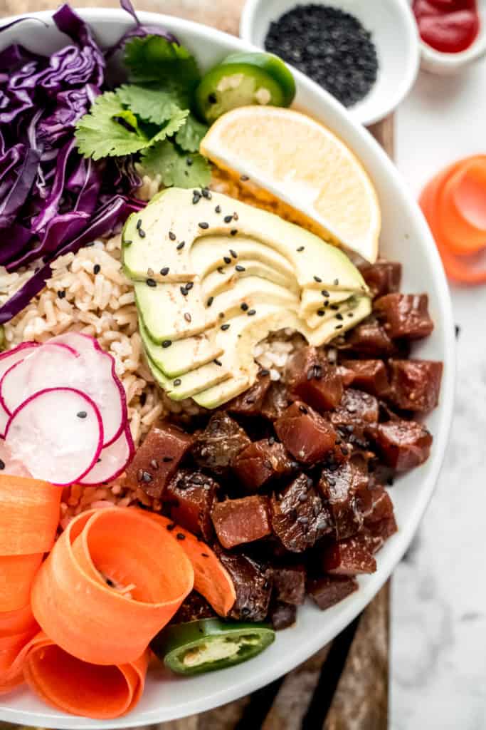 close up shot of ahi poke bowl garnished with carrot ribbons, jalapeno, radish, avocado, lemon and purple cabbage