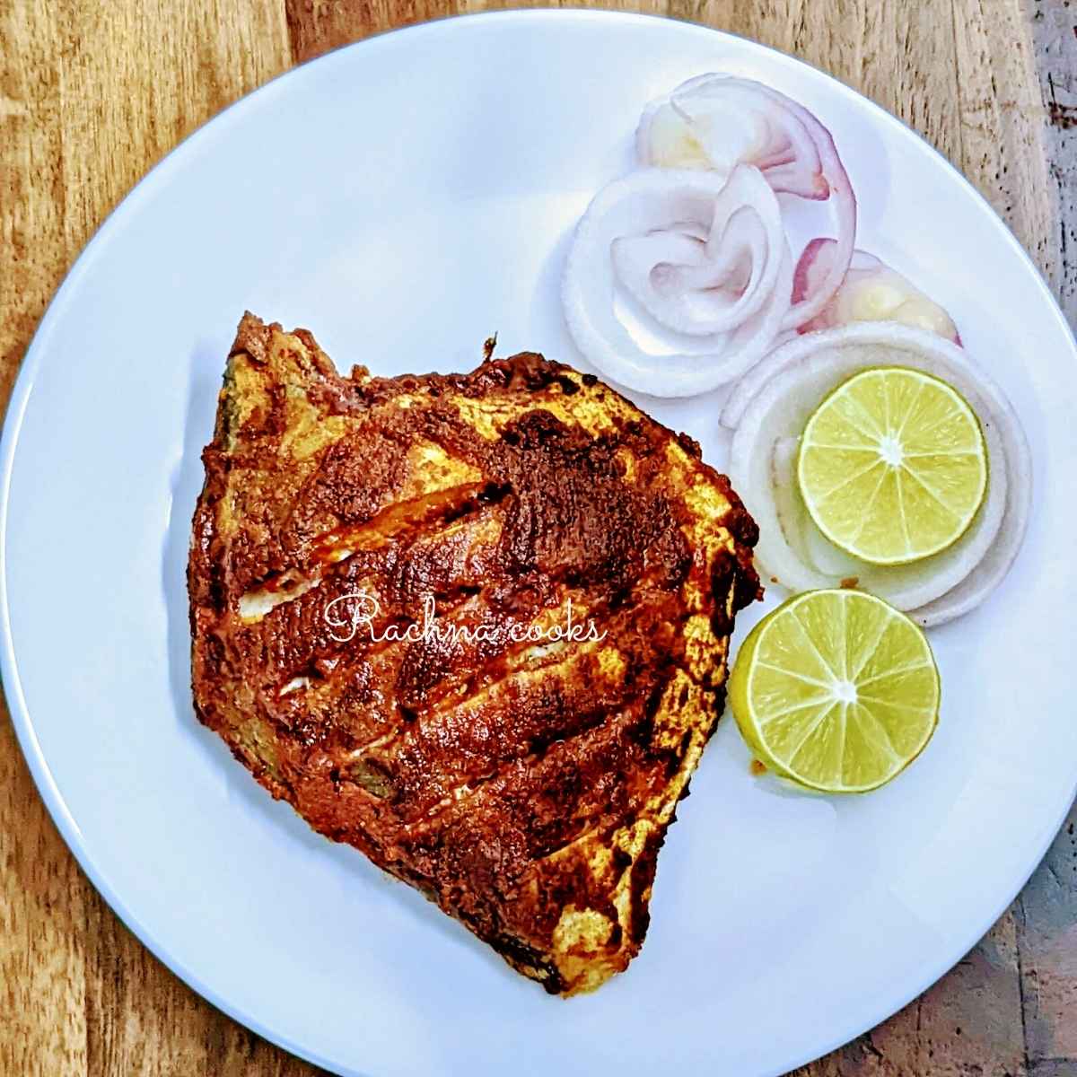 Pomfret fry in a red masala served on a white plate with lime and onion slices.