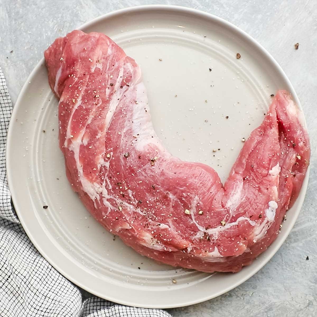 a piece of pork tenderloin on a plate seasoned with salt and pepper