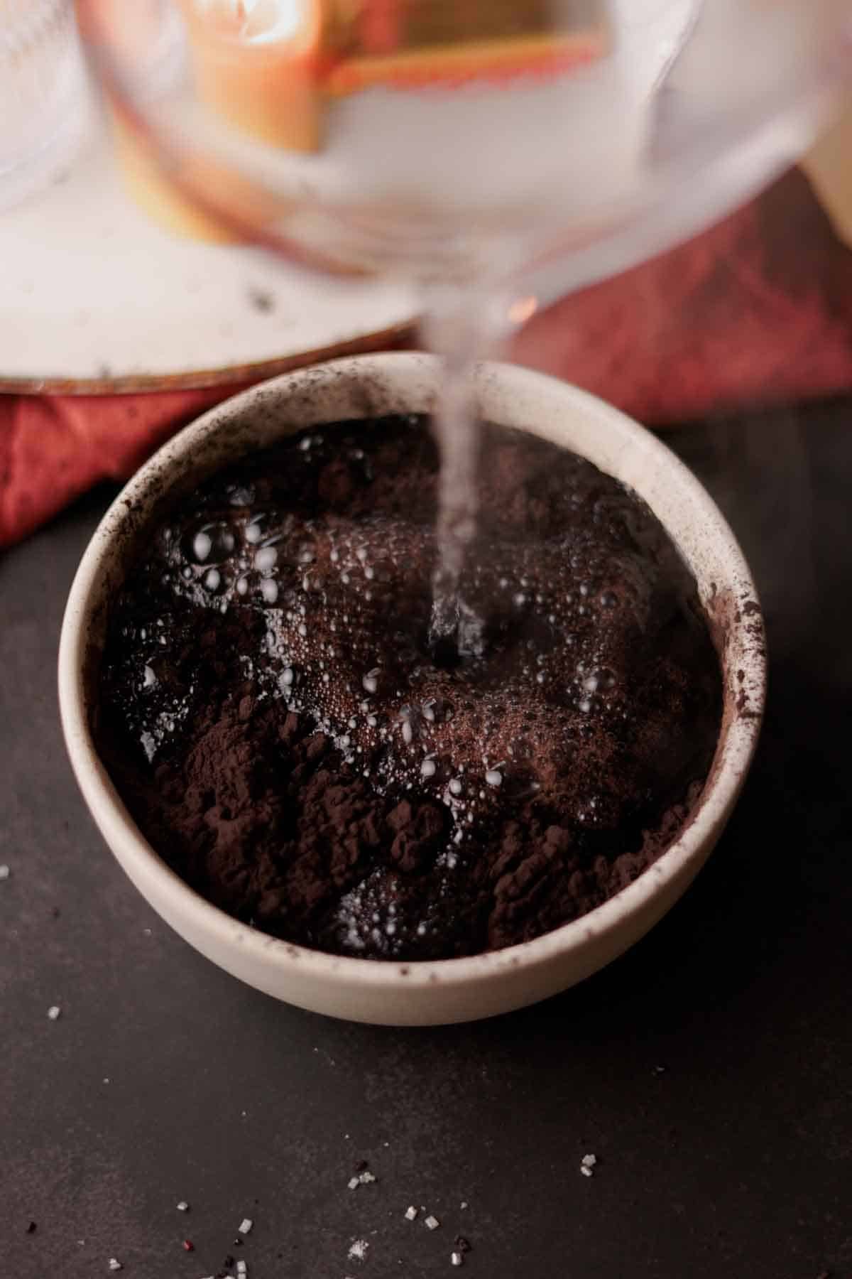 pouring hot water into a bowl with black cocoa powder