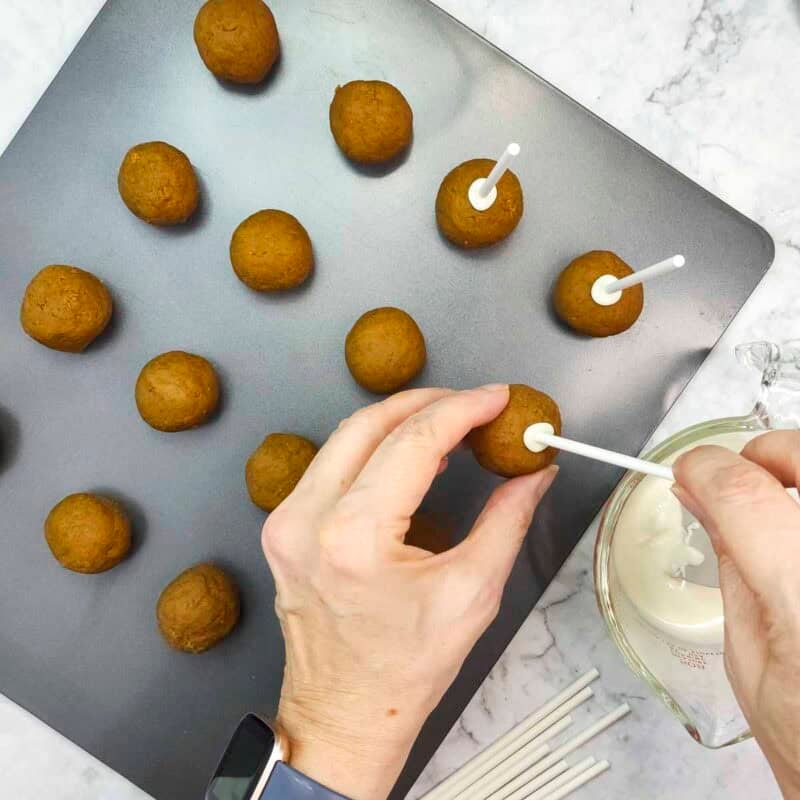 Overhead view of process shot 5 - melt about ¼ cup of the white chocolate chips in the microwave, then dip one end of each cake pop stick in the white chocolate and insert about halfway into the cake pops.
