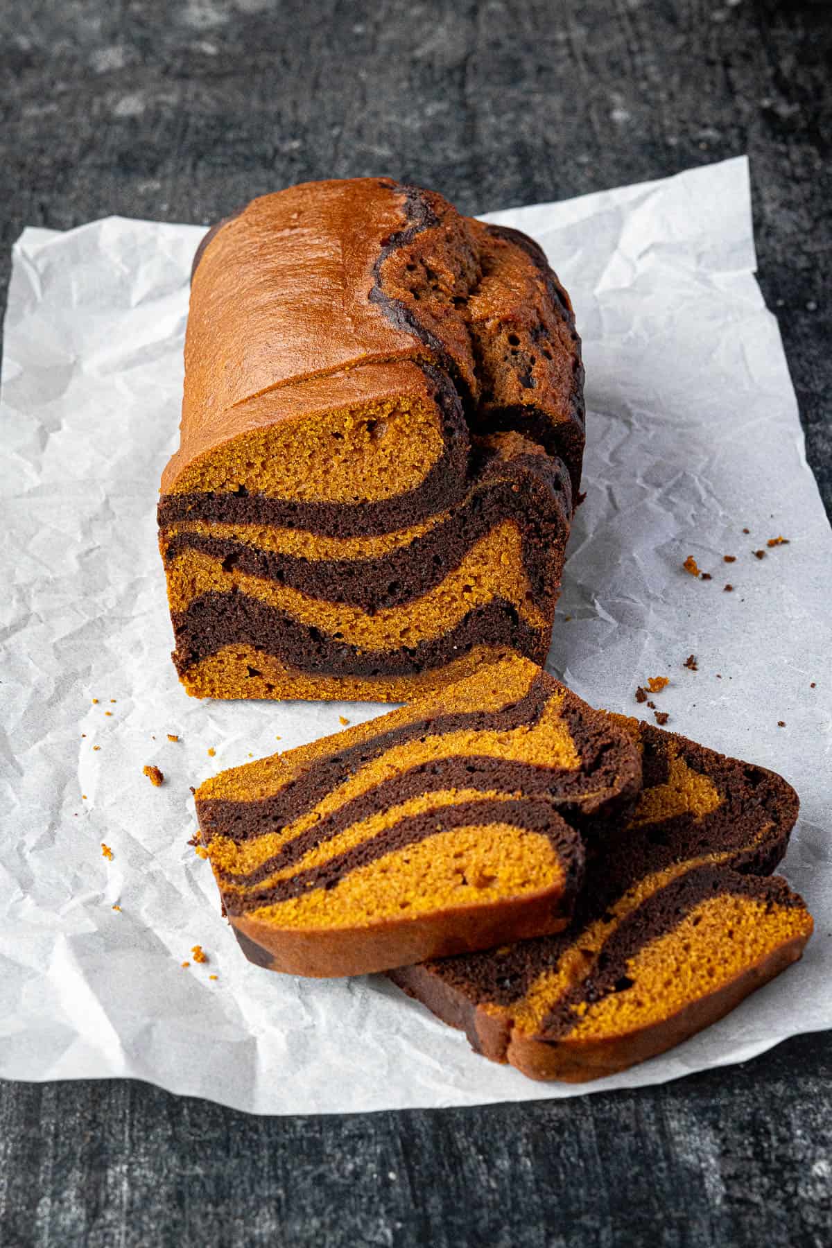 Sliced pumpkin chocolate marble bread on a sheet of baking parchment on a black surface.
