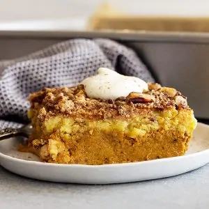 Large piece of pumpkin dump cake on a white plate topped with freshly whipped cream.