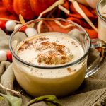Pumpkin spice hot chocolate in a glass mug. There is pumpkin spice whipped cream and a sprinkle of cinnamon on top.