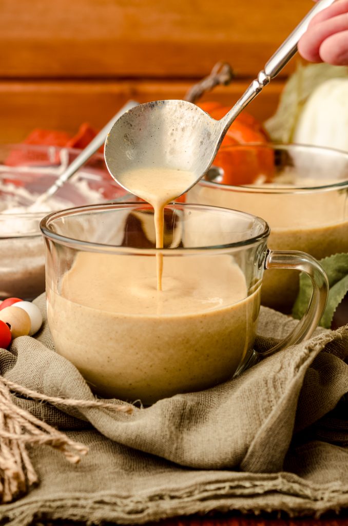 Someone is ladleing pumpkin spice hot chocolate into a glass mug.