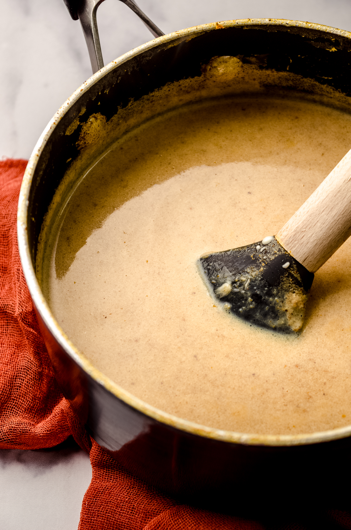 A saucepan of pumpkin spice hot chocolate with a spatula in it.