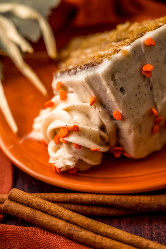 A closeup of a slice of pumpkin cake on a plate focused in on the swirl of frosting on top.