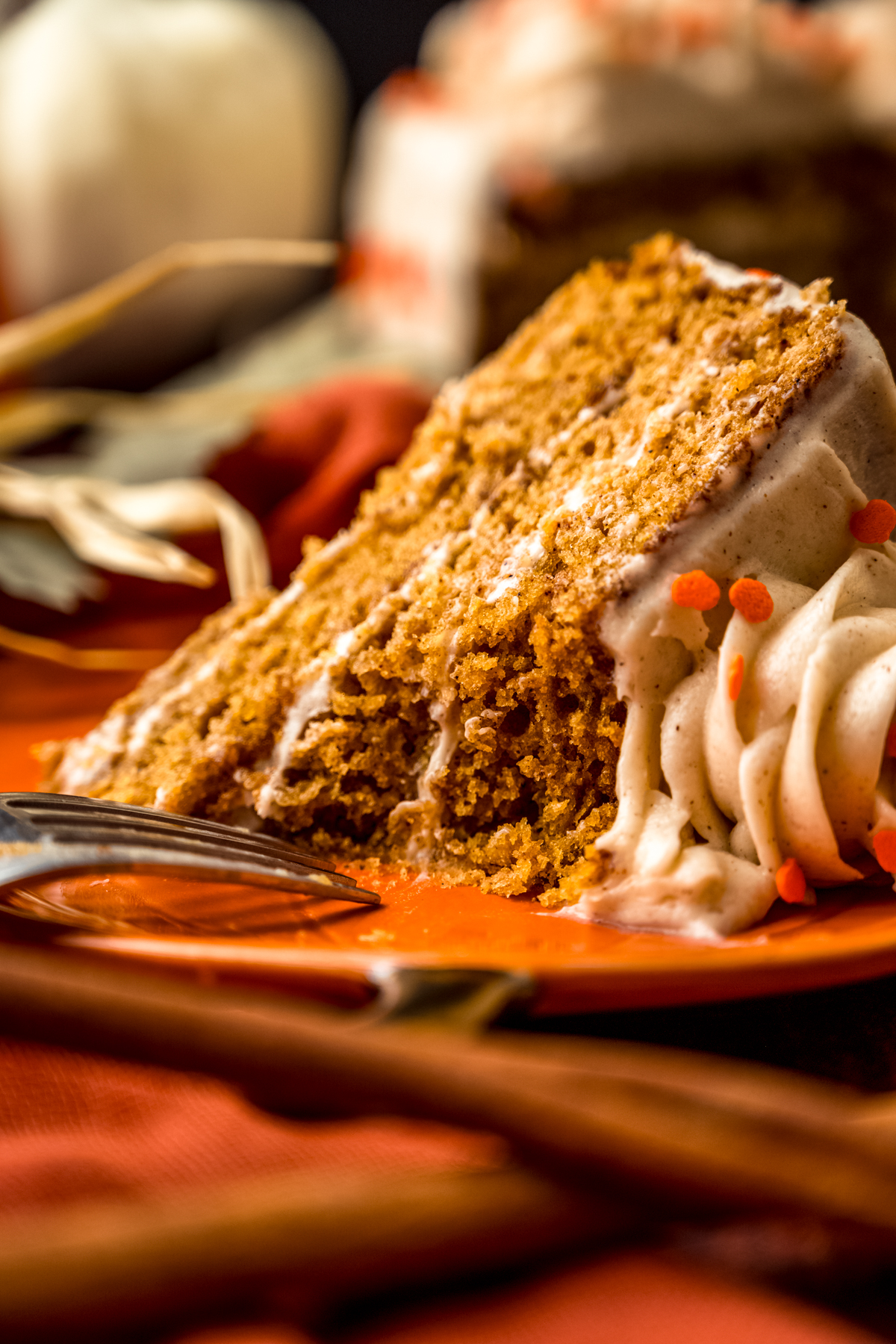 A slice of pumpkin cake on a plate with a fork and a bite has been taken from the cake.
