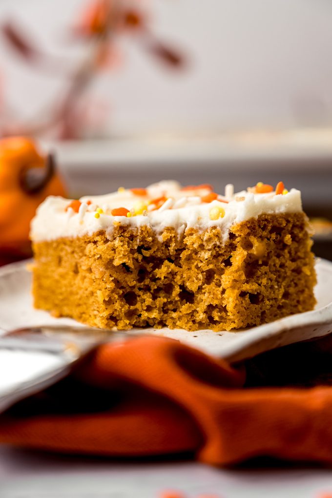 A slice of pumpkin sheet cake sitting on a plate and the cake has a bite taken out of it.