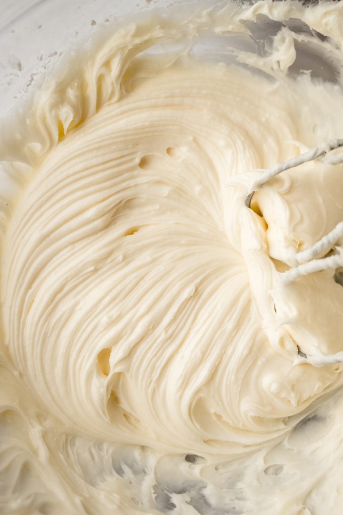Cream cheese frosting in a bowl with electric beaters.