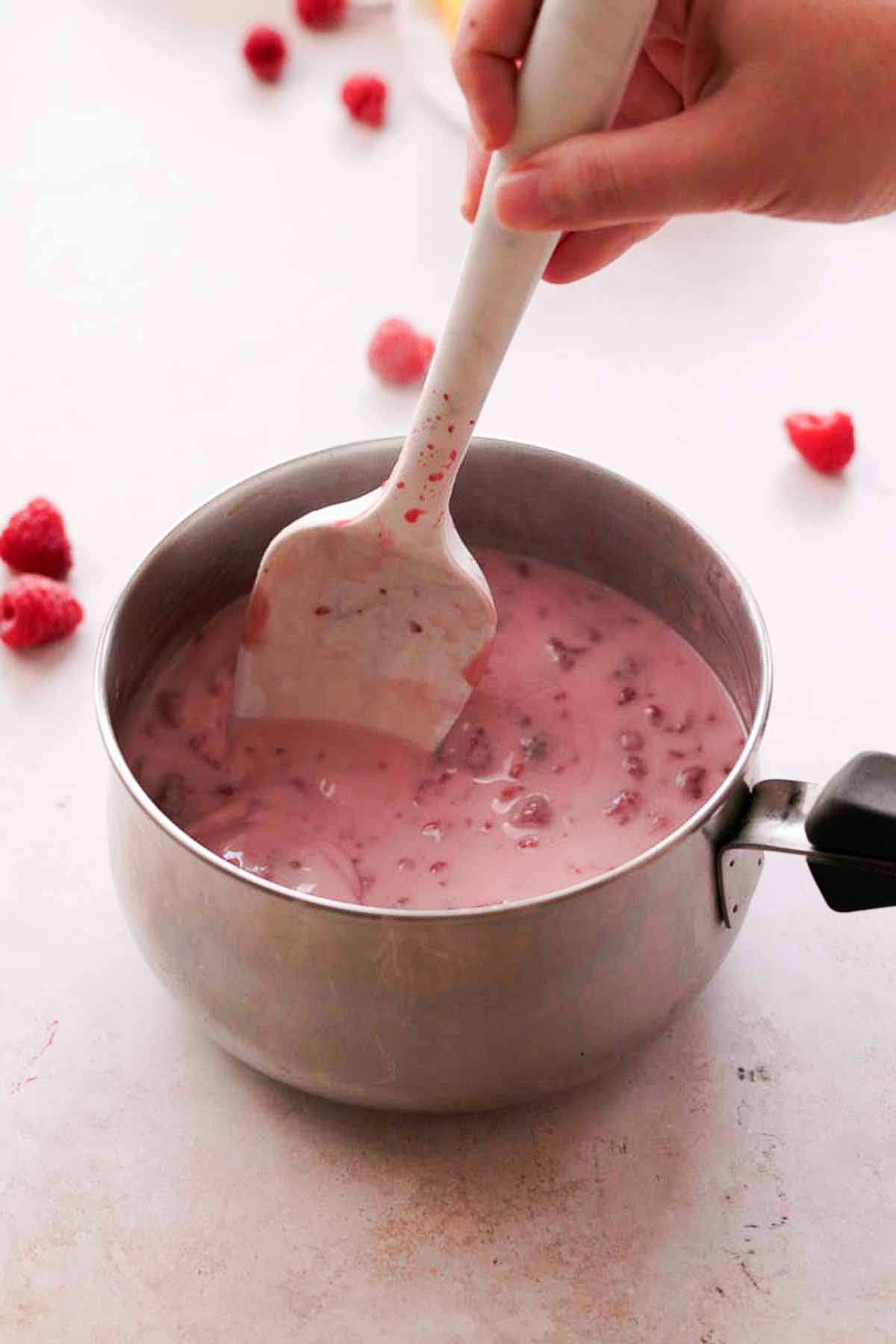 stirring raspberries and cream with silicone spatula in saucepan