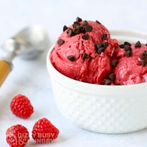Side shot of raspberry frozen yogut with chocolate chips in a white bowl with raspberries on the side.