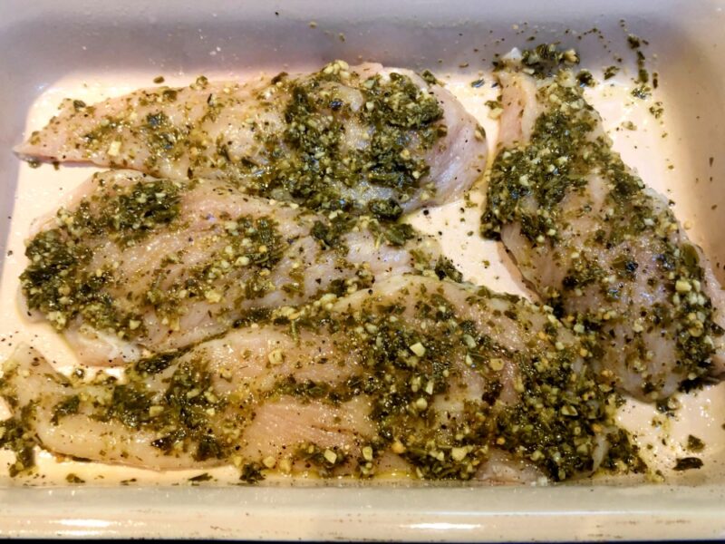 raw chicken with pesto in a dish before baking