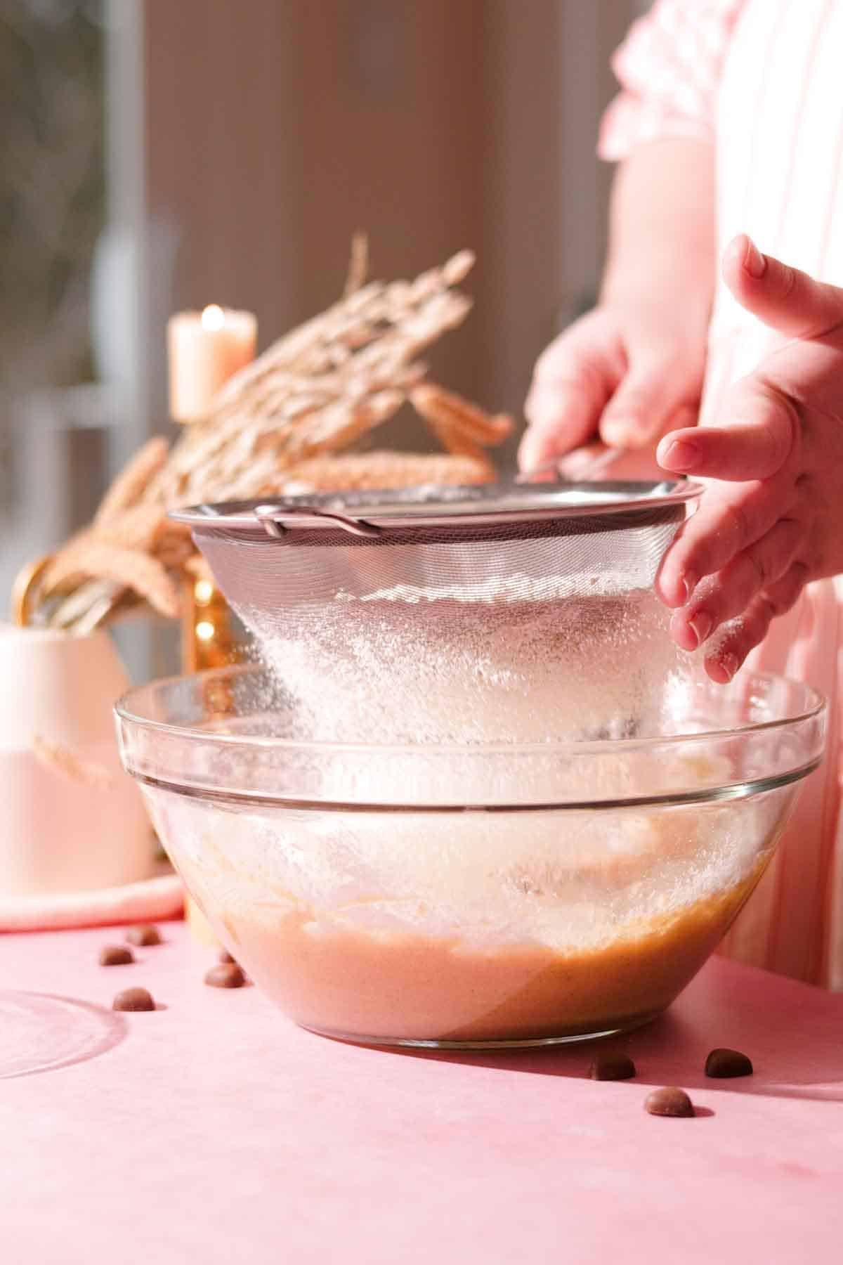 sifting dry ingredients into a glass bowl with a metal sieve