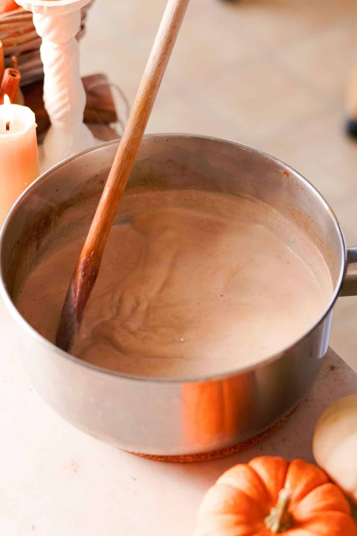 stirring chai latte in medium saucepan with a wooden spoon
