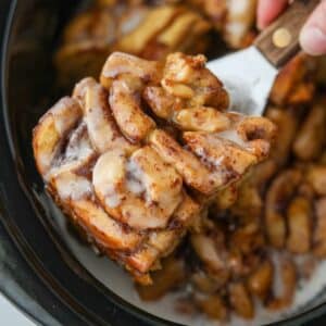 Taking a portion of crock pot cinnamon rolls from a slow cooker.