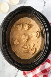 A slow cooker filled with cinnamon roll pieces and a custard mixture.