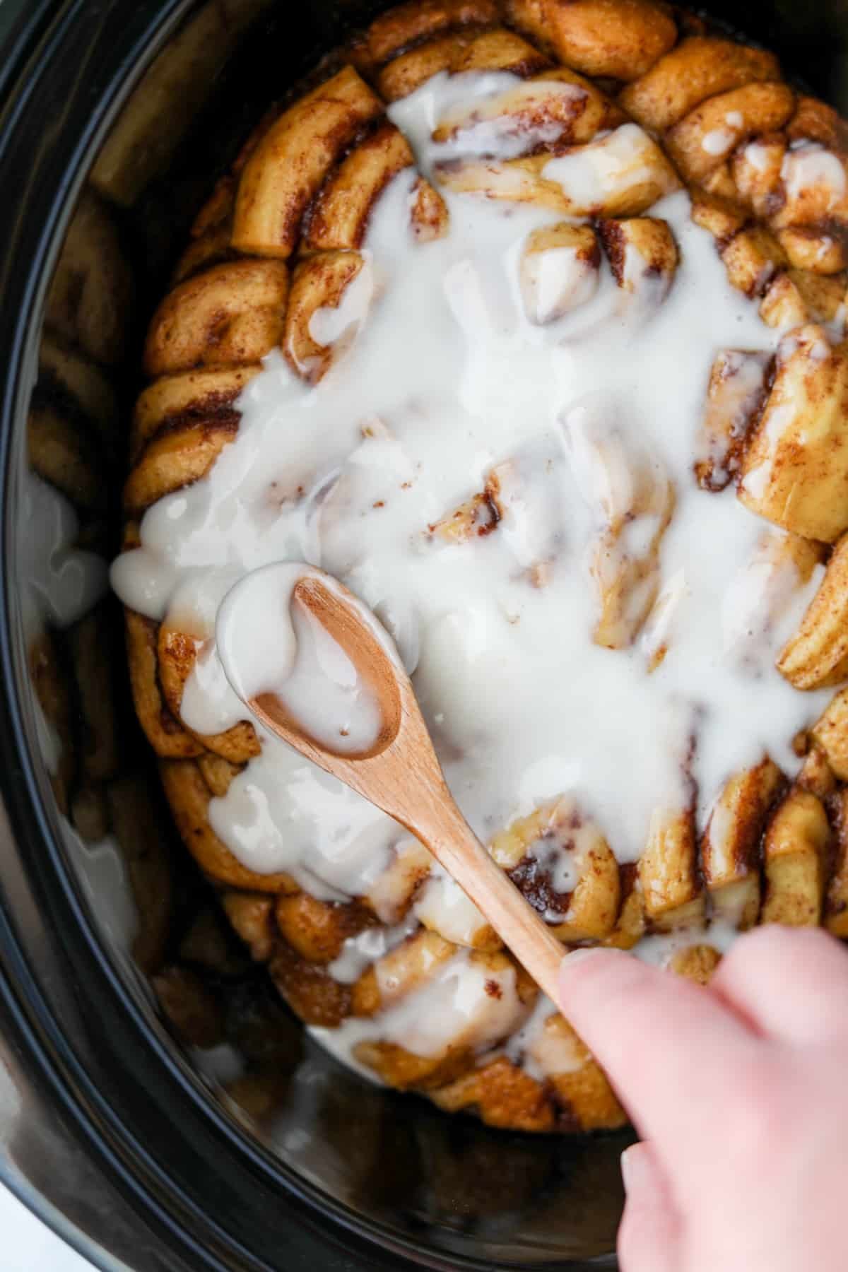 Spreading icing on top of a cinnamon roll casserole inside of a crock pot.