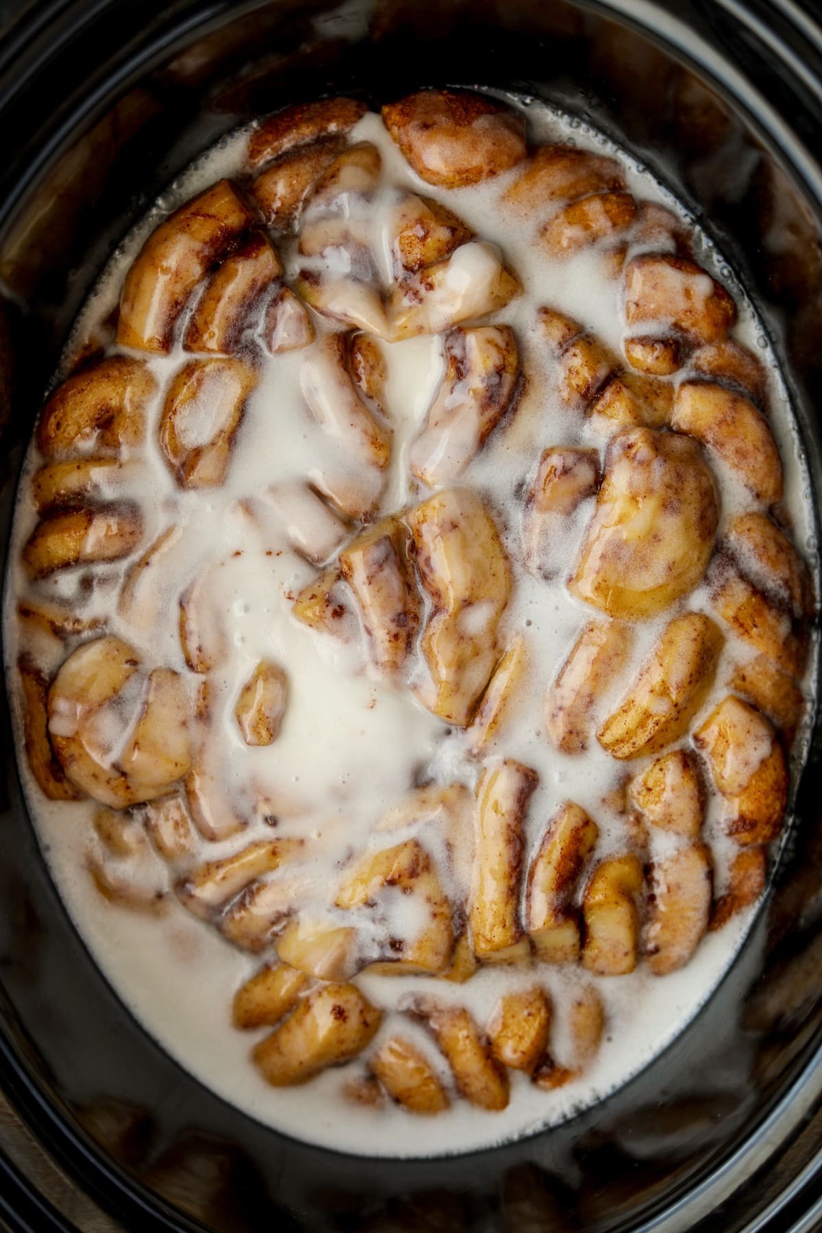 An oval crock filled with cinnamon roll casserole topped with icing.
