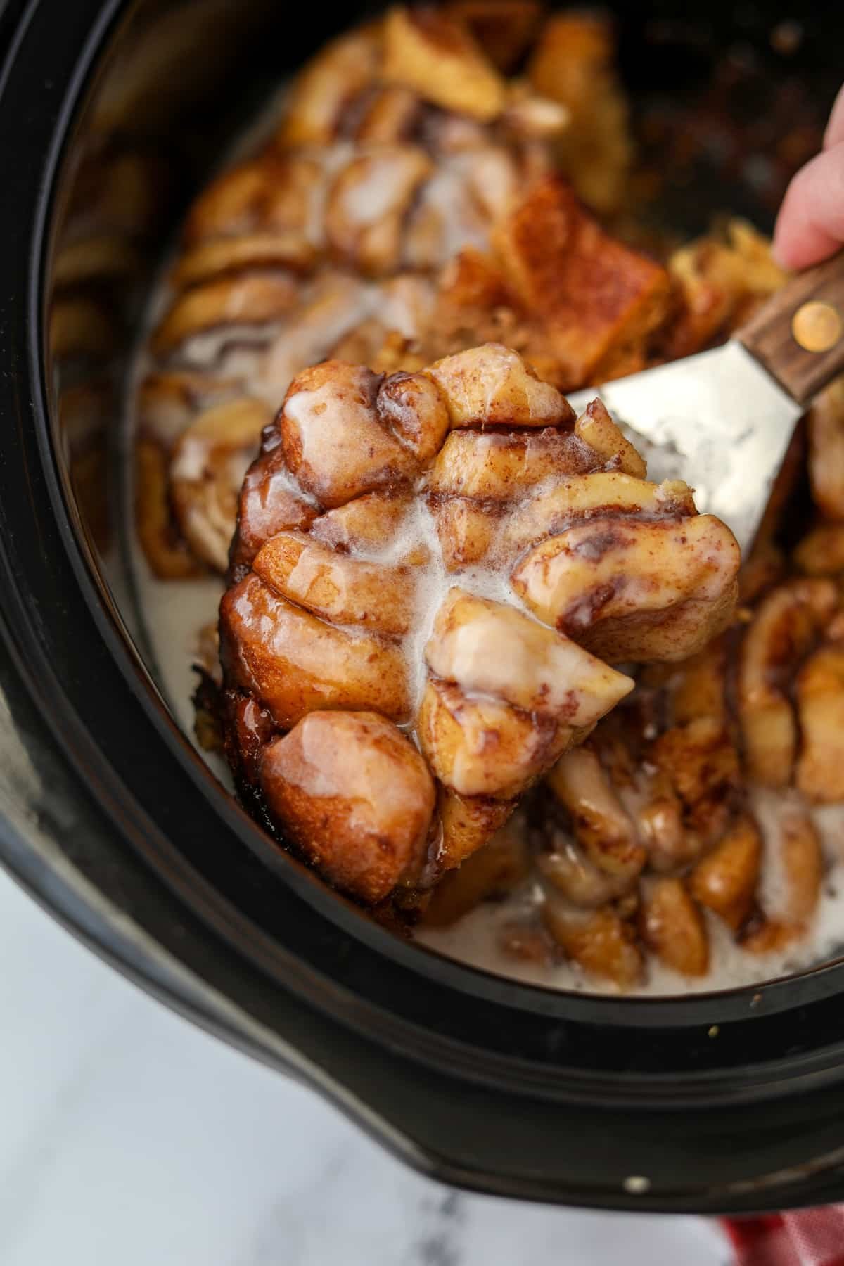 Lifting a slice of cinnamon roll bake from a crock.