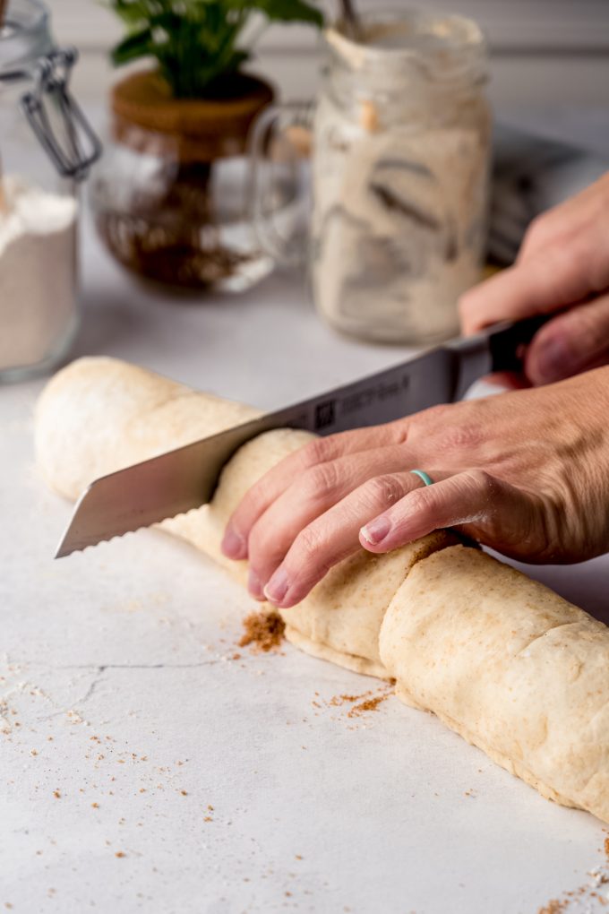 Someone is using a large knife to slice a log of cinnamon rolls into individual rolls.