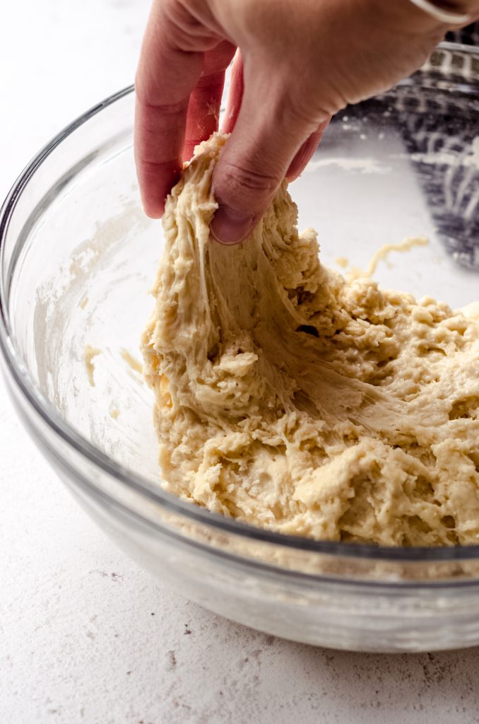 A hand performing stretches and folds on sourdough roll dough.