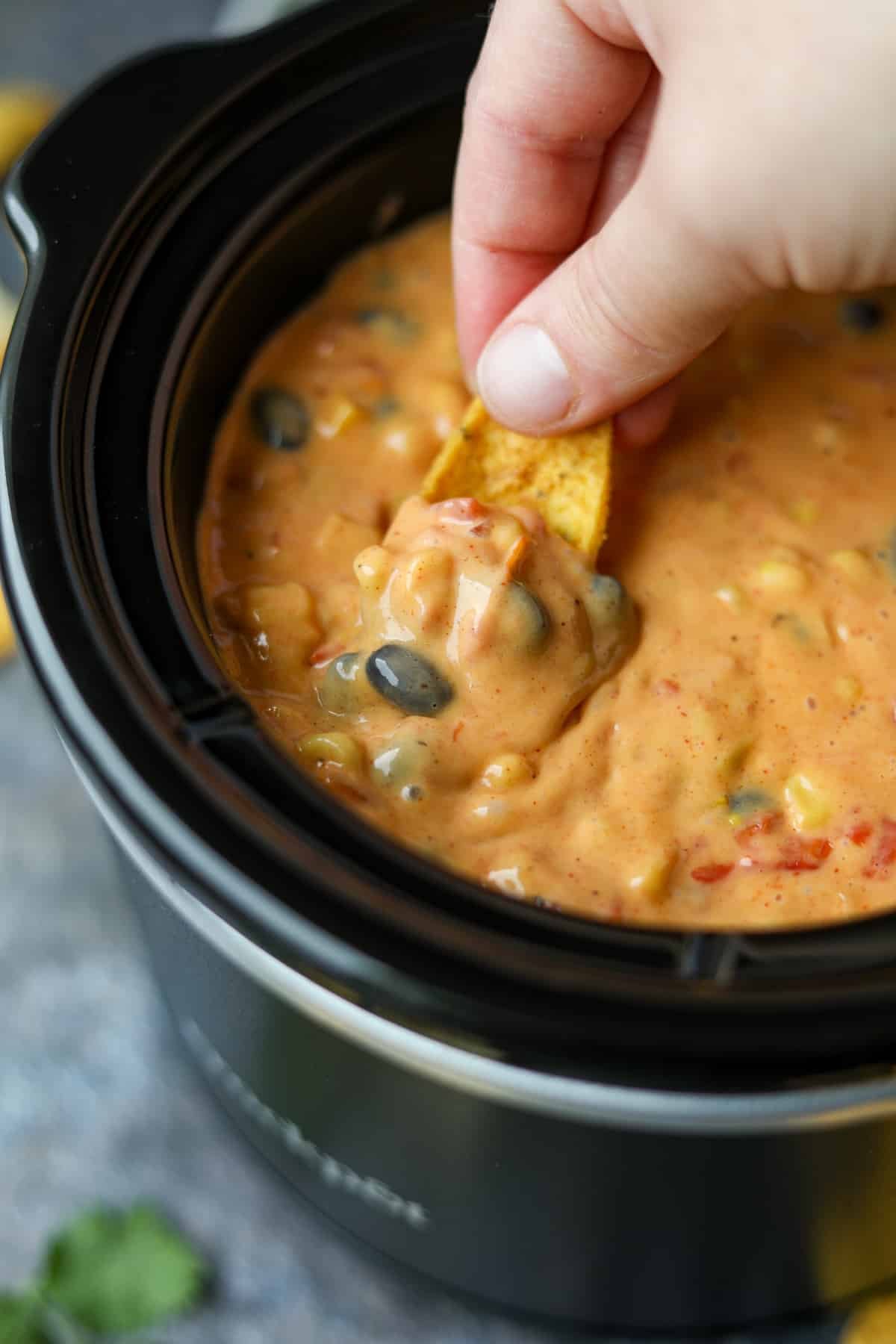 Dipping a corn chip into a slow cooker filled with Velveeta dip.