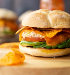 close up shot of spicy tuna avocado sandwich on wooden board with sandwiches and Doritos blurred around