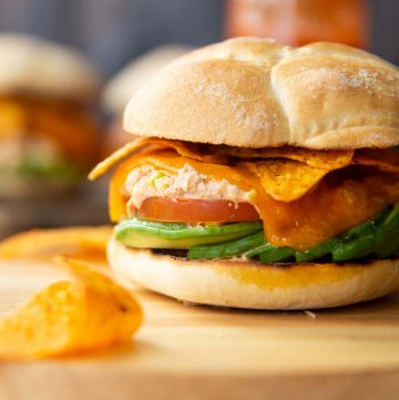 close up shot of spicy tuna avocado sandwich on wooden board with sandwiches and Doritos blurred around