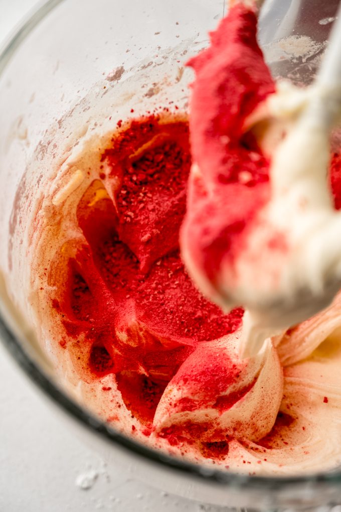 The bowl of a stand mixer with strawberry frosting in it.