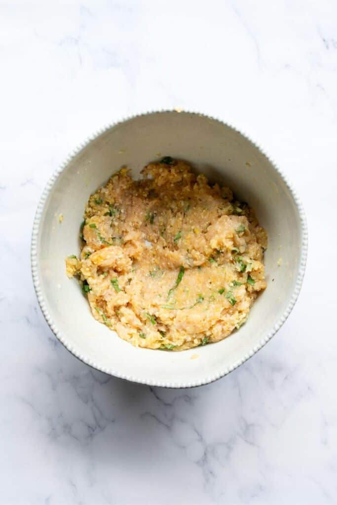 ground chicken mixture in a bowl with basil, egg, breadcrumbs oregano, salt, pepper, and parmesan cheese