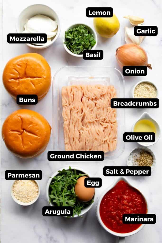 all ingredients in chicken parm burgers in small bowls including ground chicken, marinara, egg, mozzarella, parmesan, breadcrumbs, salt, pepper, olive oil and buns