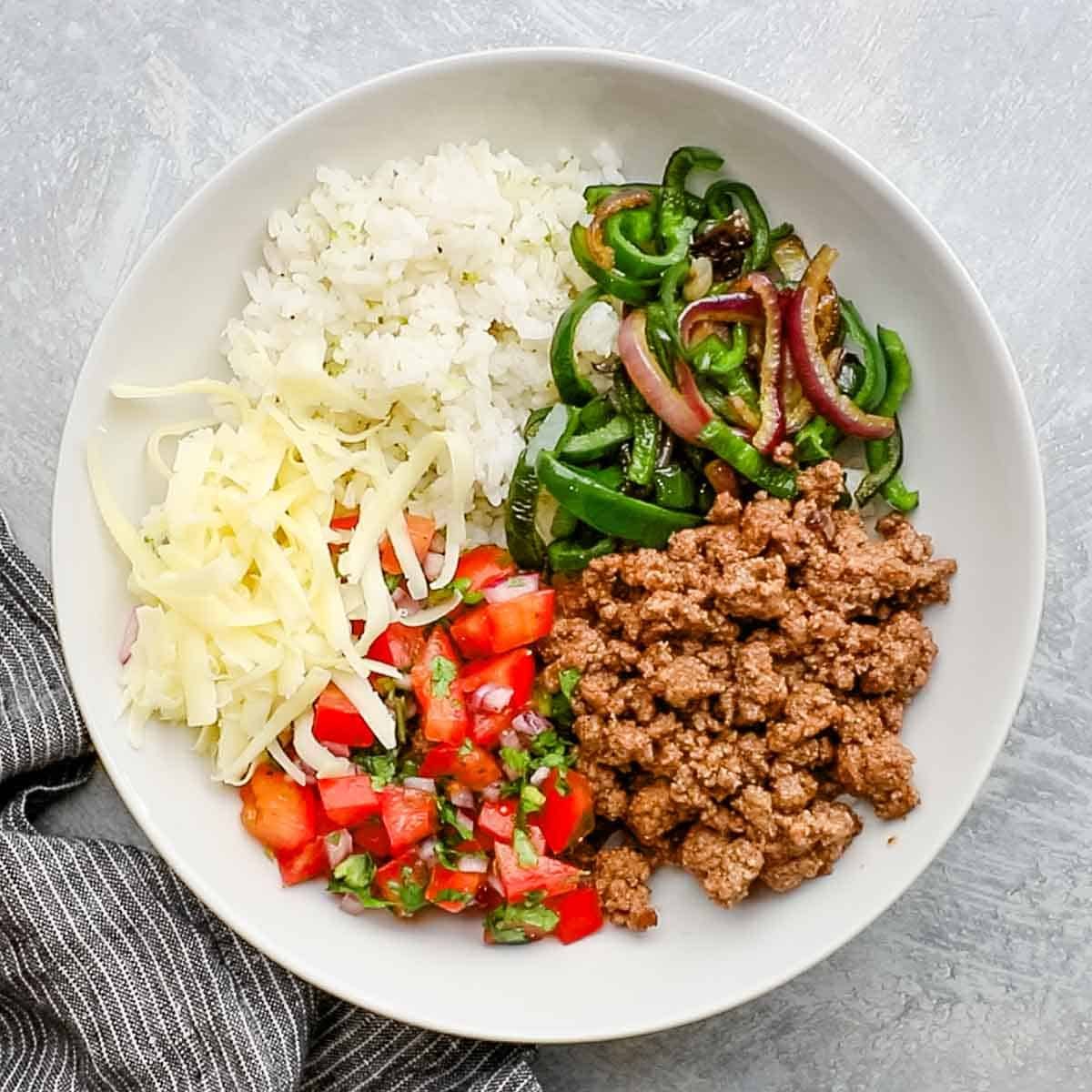 ground beef, peppers, pico, and cheese added to a bowl of rice