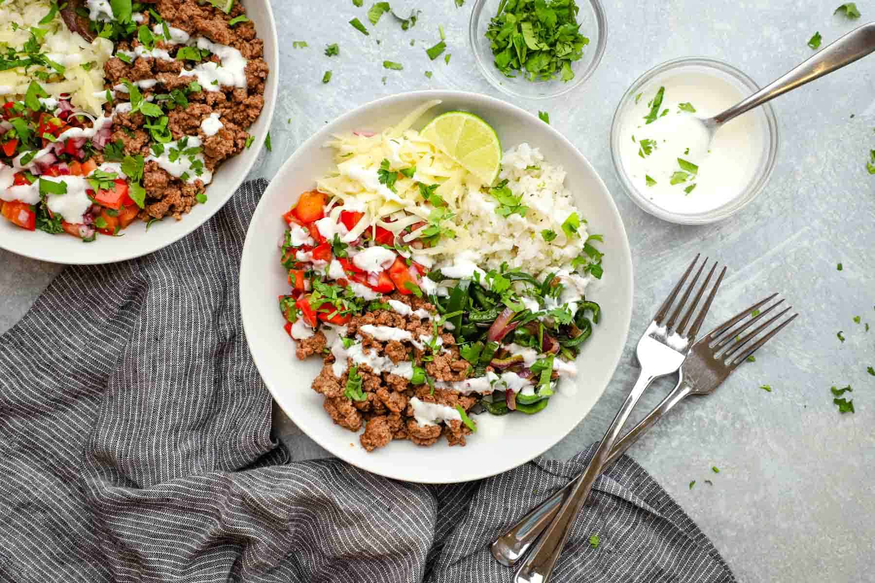 a rice bowl topped with ground beef, shredded cheese, lime crema, onions and peppers