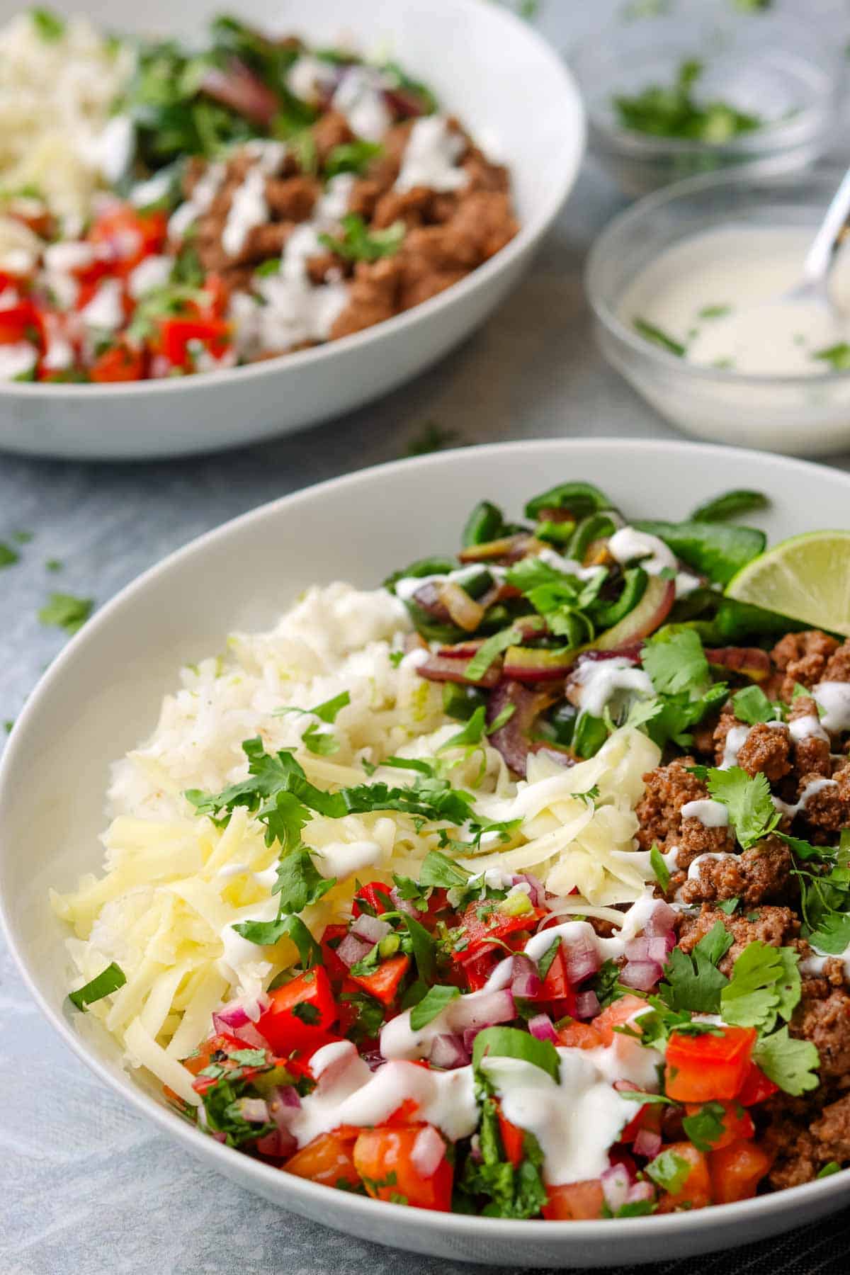 a rice bowl topped with ground beef, shredded cheese, lime crema, onions and peppers