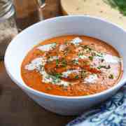 Photo of a bowl of tomato, lentil and squash soup with vegan cream swirled on top and chopped chives.
