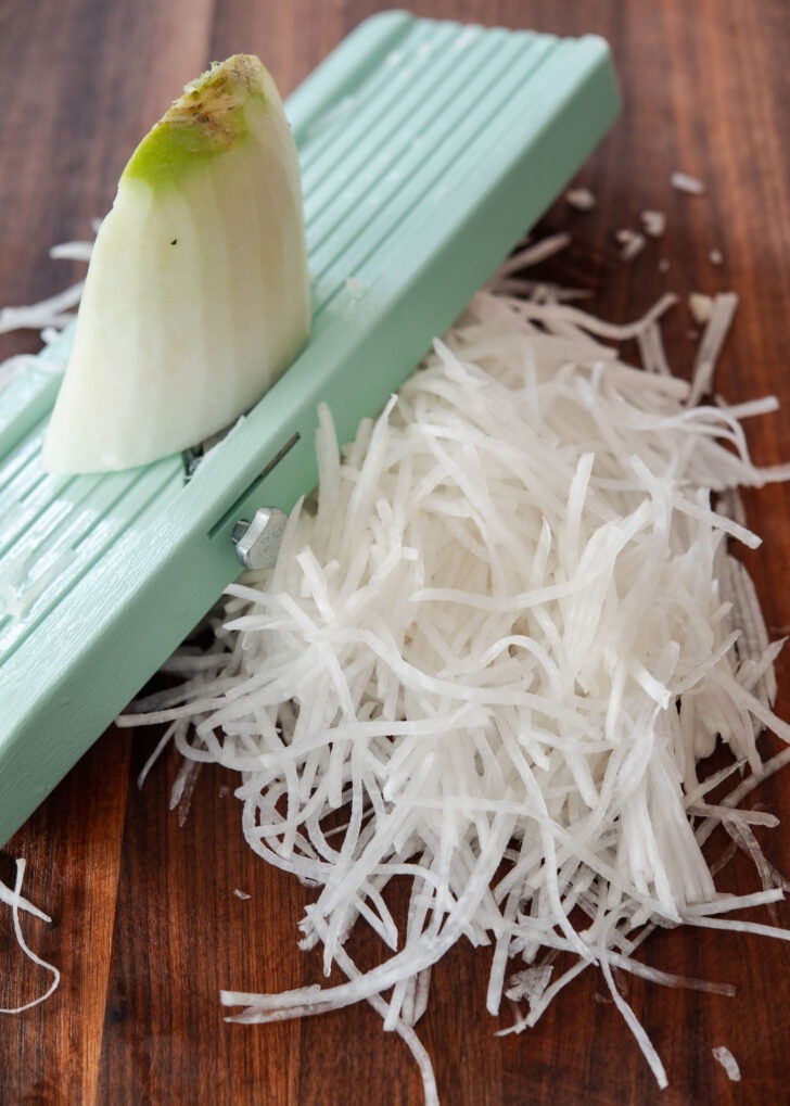 Shredding Korean radish into thin strips using mandolin slicer.