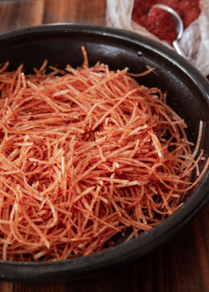 Coating shredded radish with Korean chili flakes (gochugaru).