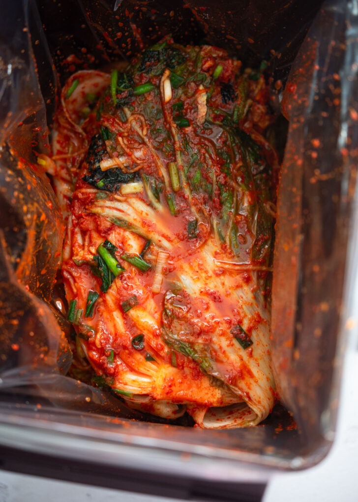 Pouring the seasoning paste and water onto kimchi in a container.