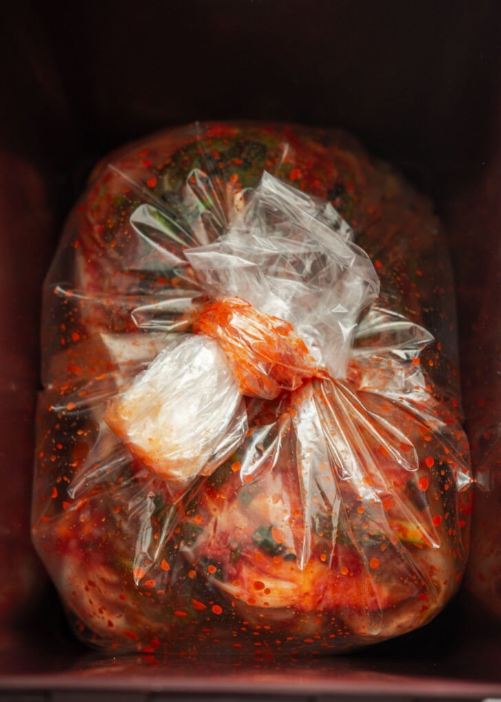 A plastic bag with kimchi inside tied tightly in a container.