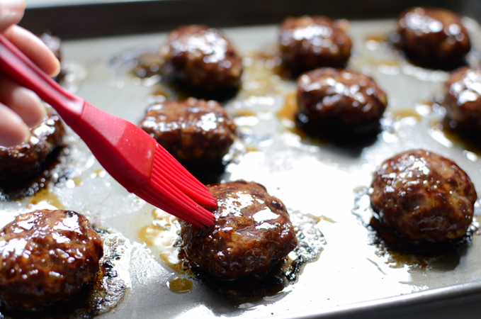 Brush coating yujang glaze on cooked beef patties on a baking sheet.